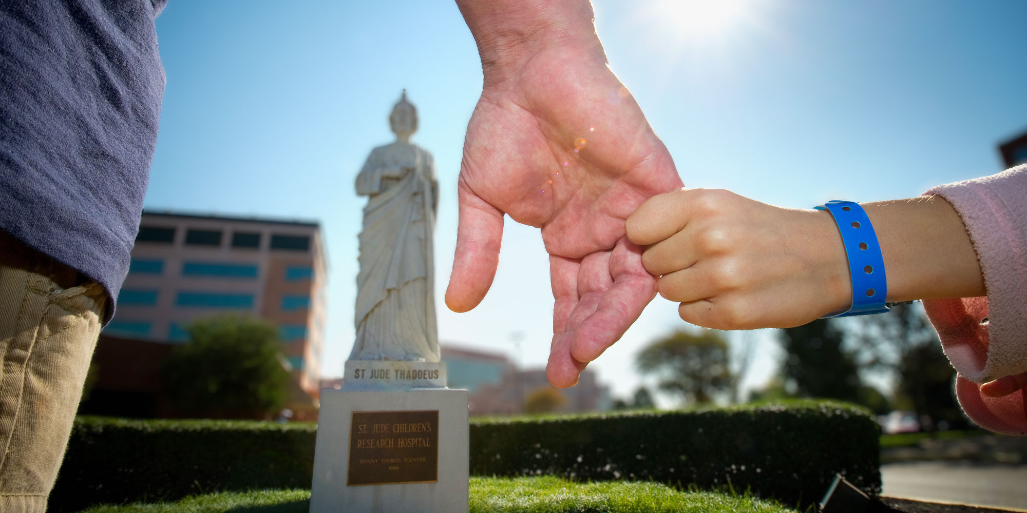 Parent and child holding hands at monument in honor of St. Jude Thaddeus. Jude is the Patron Saint of Hope and impossible causes and one of Jesus' original twelve Apostles. He preached the Gospel with great passion, often in the most difficult circumstances. Through the power of the Holy Spirit, he made profound differences in people's lives as he offered them the Word of God.